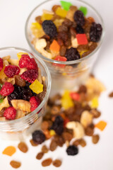 muesli dessert in glass with yogurt and candied or dried fruits with raspberries on top, isolated on white background. raisins, nuts and candied fruits nearby. Granola breakfast