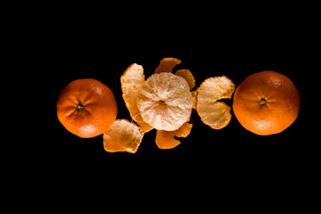 The ripe fruit of the citrus plant mandarin, peeled and also not peeled, on a black background