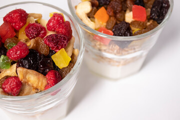 muesli dessert with yogurt and candied or dried fruits with raspberries on top in glass isolated on white background. Granola breakfast