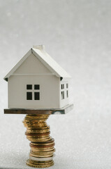 miniature metal house standing on a high stack of golden coins