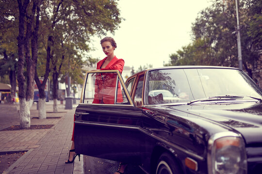 Beautiful young woman wearing red costume while standing near retro car