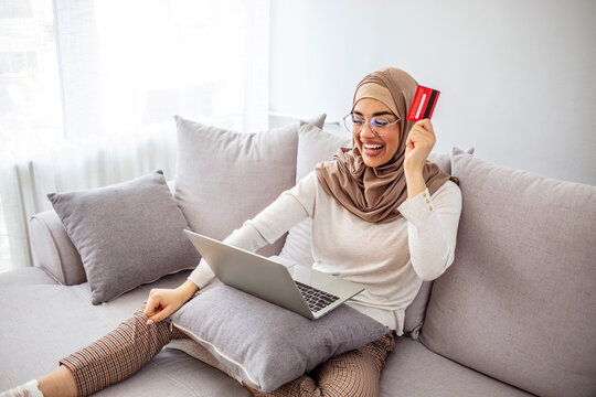 Easy payments. Smiling arabic woman in headscarf using laptop and credit card at home, paying for utilities online, free space. Online Credit Concept.