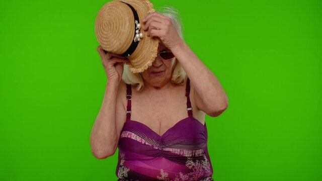 Senior woman traveler tourist takes money from hat, counting bunch of dollars cash. Income, saving, credit for vacation. Elderly grandmother in swimsuit ready for summer holiday sea trip. Chroma key