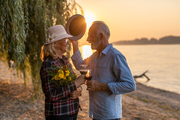 The happy senior couple is drinking wine and enjoying the sunset on the river.	