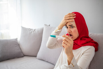 Unsmiling Muslim woman holding her pregnancy test. Bad mood. Unhappy young woman sitting and holding her pregnancy test. Worried Muslim girl after looking a pregnancy test