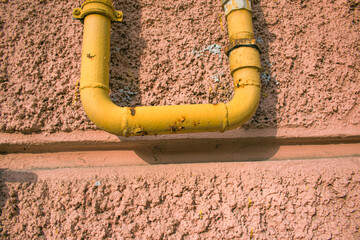 A yellow gas pipe with a coupler runs along the facade of a multi-story building. The house is...