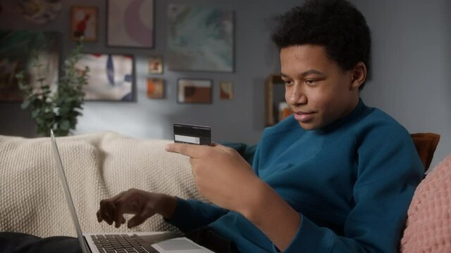African American black teenager man paying with credit card online making orders via Internet. High school student holding plastic card making transaction using mobile banking application
