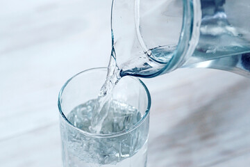Pouring water from jug into glass on wooden background. Pouring fresh water from a jug into a glass. Health and diet concept
