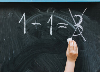 Girl, child writes and incorrectly solves a mathematical equation, a problem on a wooden black...
