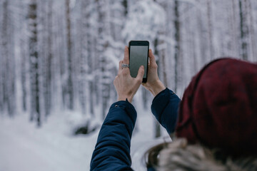 Young beautiful happy girl in red winter knitted hat takes photo in winter forest. Travel and active life concept. Outdoors 