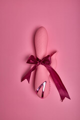 Flat lay pink cute dildo vibrator isolated on pink background , dildo vibrator, accessory for sex games wrapped in red bow as present