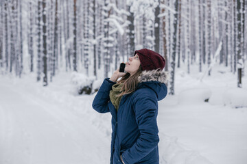 Fototapeta na wymiar Beautiful girl calls a taxi in the winter forest