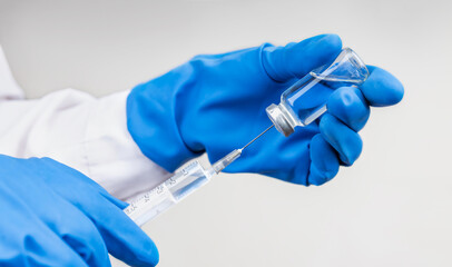 A bottle of COVID-19 vaccine and a syringe with a needle for injections for coronavirus infection in the hand of a doctor in a nitrile glove on a white background. Close-up. Concept fighting