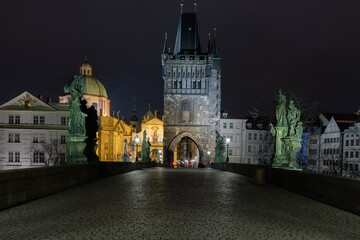 view of the bridge tower and cobblestone walkway on Charles Bridge and lighted lanterns at night in the center of Prague