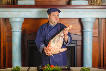 Half legth shot of thoughtful male chef, holds very big red raw piece of meat, needs to chop for...