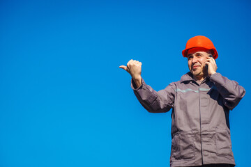 Construction worker in a helmet against the blue sky talking on the phone. Contractor control...