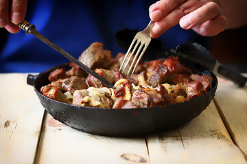Soft focus. Frying pan with fried meat. The man is eating fried meat pieces.