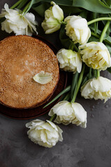 A stack of fried pancakes on a table with tulips. View from above.