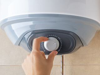 Woman hand rotates water heater temperature adjuster to the Eco position for economical use of electricity. Modern home appliances with energy saving mode. Domestic life.