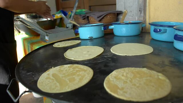 Cook flattening corn dough next to a comal with handmade tortillas