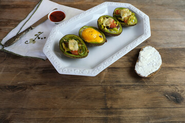 baked avocado stuffed with egg, vegetables, lie on a white dish, bread smeared with curd mass, linen napkin with embroidery, concept of post-holiday detox, diet, healthy food