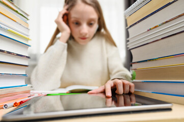 A schoolgirl uses a tablet while learning. Selective focus on the finger of the control tablet. Distance learning concept.