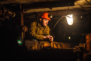 A tired miner in a coal mine looks at the light. Work in a coal mine. Portrait of a miner. Copy...