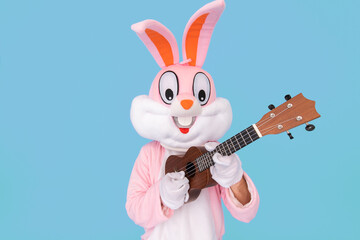 Fototapeta na wymiar Positive funny musician guitarist plays music by ukulele or Hawaiian guitar isolated on blue. Easter bunny or rabbit or hare celebrates Happy easter