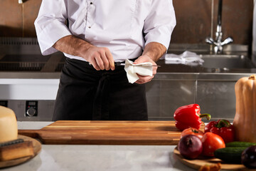 cooking, food and home concept. cropped chef wipes knife before cutting food in kitchen