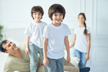 Portrait of happy little latin boy smiling at camera while having fun his father and siblings at home