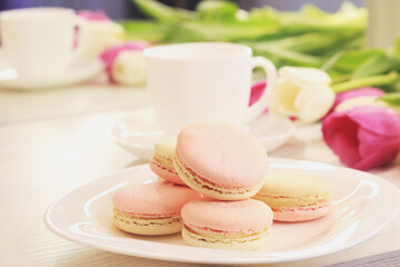 Tasty macaroons and flowers on light background