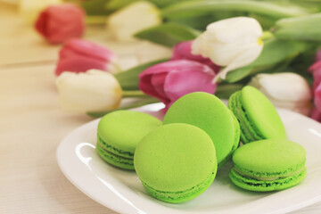 Tasty macaroons and flowers on light background