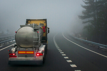 Tank truck driving down the highway on a foggy day, seen from behind.