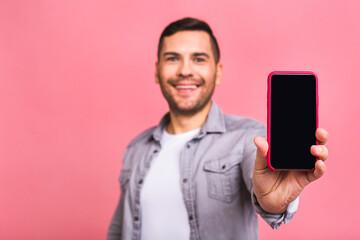 Happy winner! Young handsome man showing smartphone screen isolated over pink background with unexpected face. Human emotions, facial expression concept.