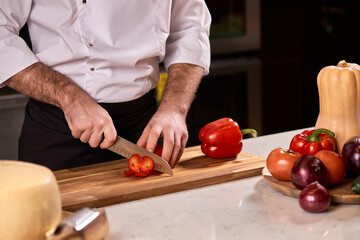 chef hand cutting pepper on cutting board in restaurant kitchen. cooking, food and restaurant concept