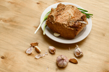 baked meat on a plate, green onion and garlic on wooden background, home cooking
