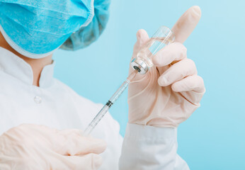 Doctor making vaccination in protective mask and gloves. Covid 19 Vaccine injection in glass vial bottle and syringe, medicine liquid in doctor hand on blue background