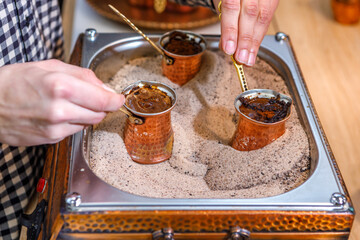 The barista brews natural coffee in copper turks on the sand. The process of making a drink.