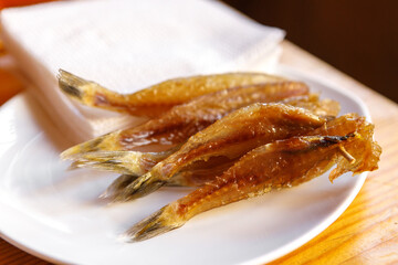 Dried fish strung on a wooden skewer lies on a plate.