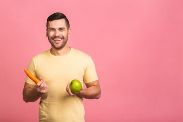 Diet concept. Portrait of man isolated on a pink background holding carrot and apple. Vegetarian preparing a meal. Smiling guy loves fruits and vegetables.