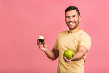 Joyful young Caucasianman in casual made wrong choice deciding between cake and fresh green apple....