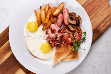 Top view on full American Breakfast on white plate in restaurant, copy space. fried eggs, roasted bacon, fries and vegetables prepared by professional chef cook. european cuisine concept