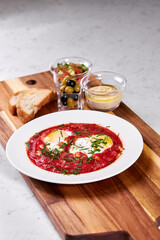 Dish of eggs in tomato sauce served with bread, olives on wooden board. Traditional Russian cuisine in restaurant. Close-up