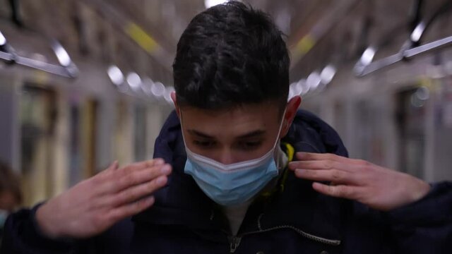 Close-up Of Teenage Boy Putting On Face Mask During Ride In Underground Metro Car. Masked Teen Passenger Dressed In Jacket Riding In Subway Train During Covid-19 Pandemic, Safety In Public Transport