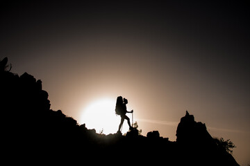 gorgeous view of female silhouette with tourist equipment walking along rocky path against sun