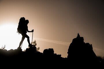 side view of female silhouette with tourist equipment walking along rocky path against sun