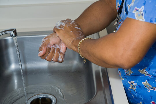 African-American nurse woman washing her hands in a stainless steel sink at a hospital or medical clinic