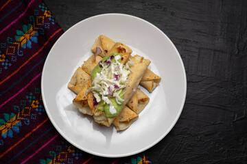 Fried tacos called flautas with guacamole and cabbage on dark background. Mexican food