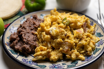 Scrambled eggs with green sauce and refried beans on white background. Mexican food