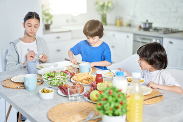 Obraz na płótnie Canvas Foodies. Adorable little hispanic kid having breakfast together with his siblings. Children enjoying meal, sitting at the table in kitchen at home